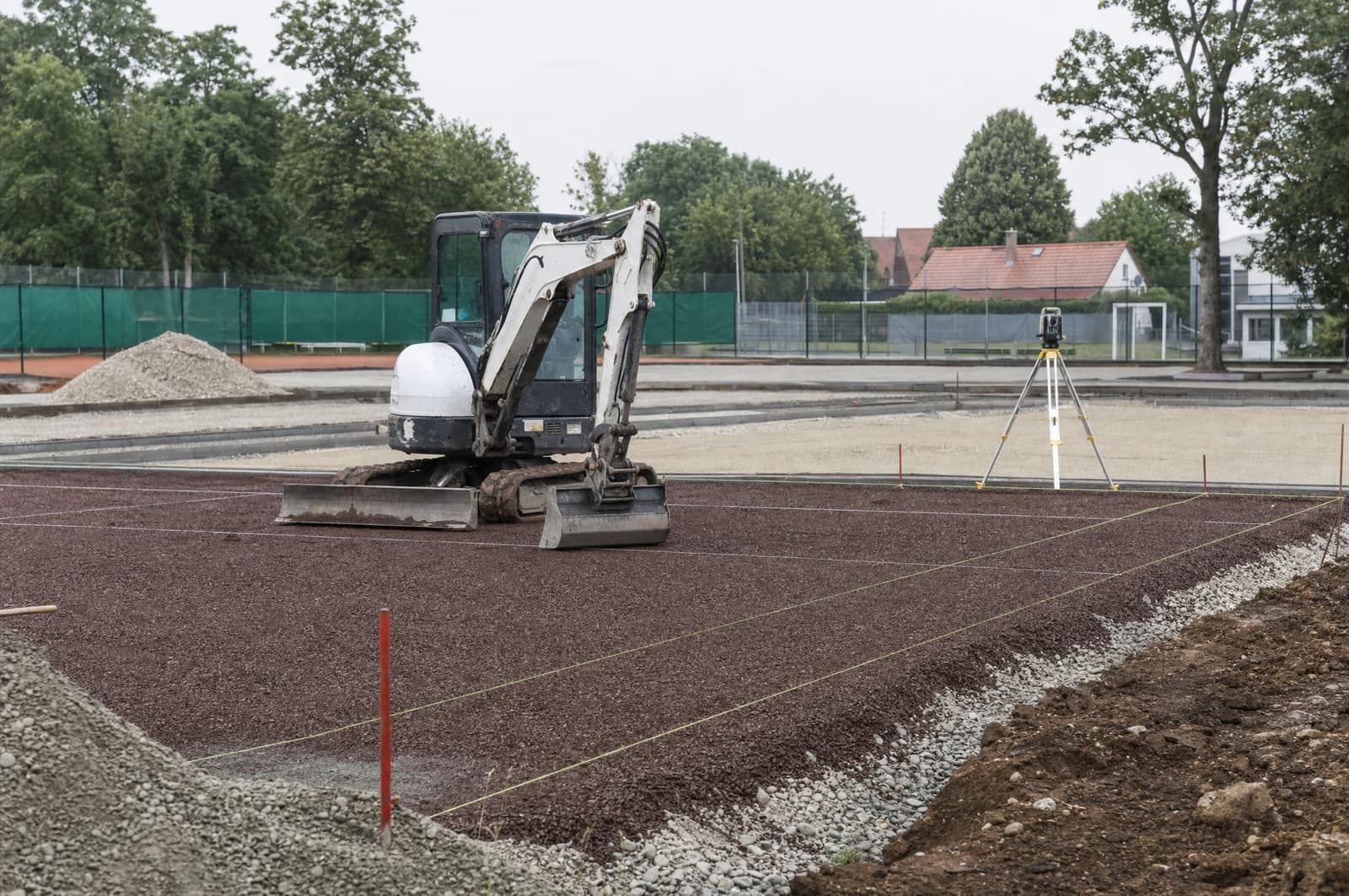 Baugrube eines neuen Tennisplatzes mit sichtbarem Schichtaufbau und Schnurgerüst